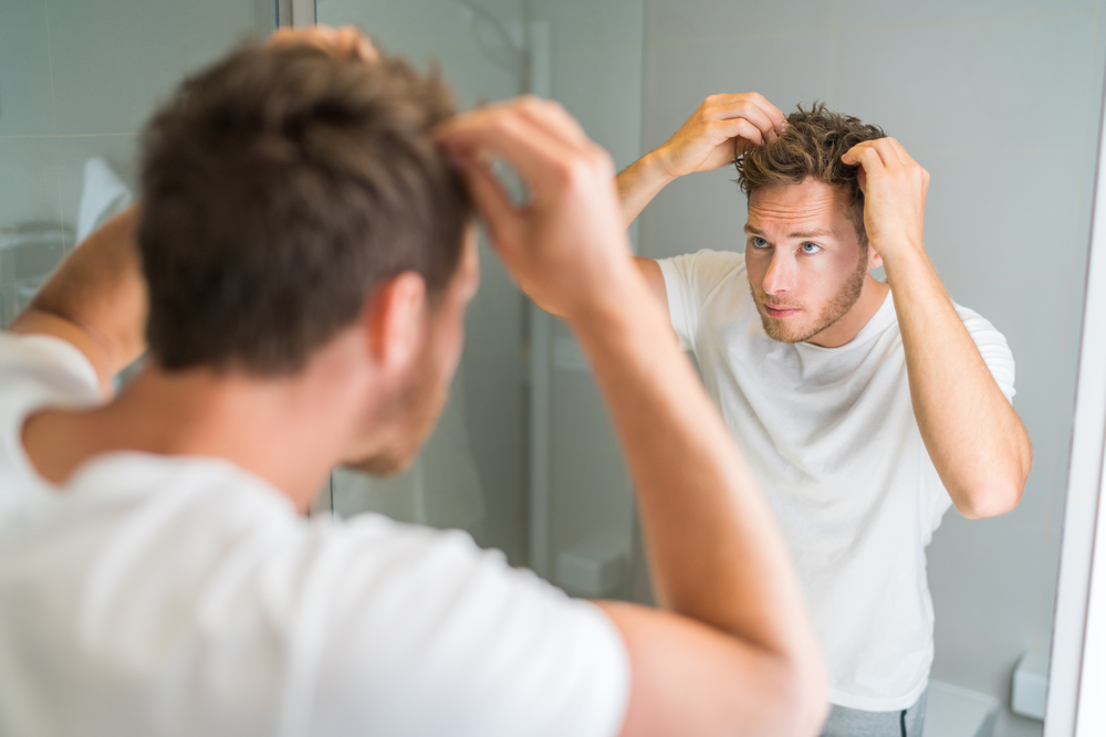 Man die een scalp moisturizer nodig heeft voor mannen met vet haar kijkt in een spiegel
