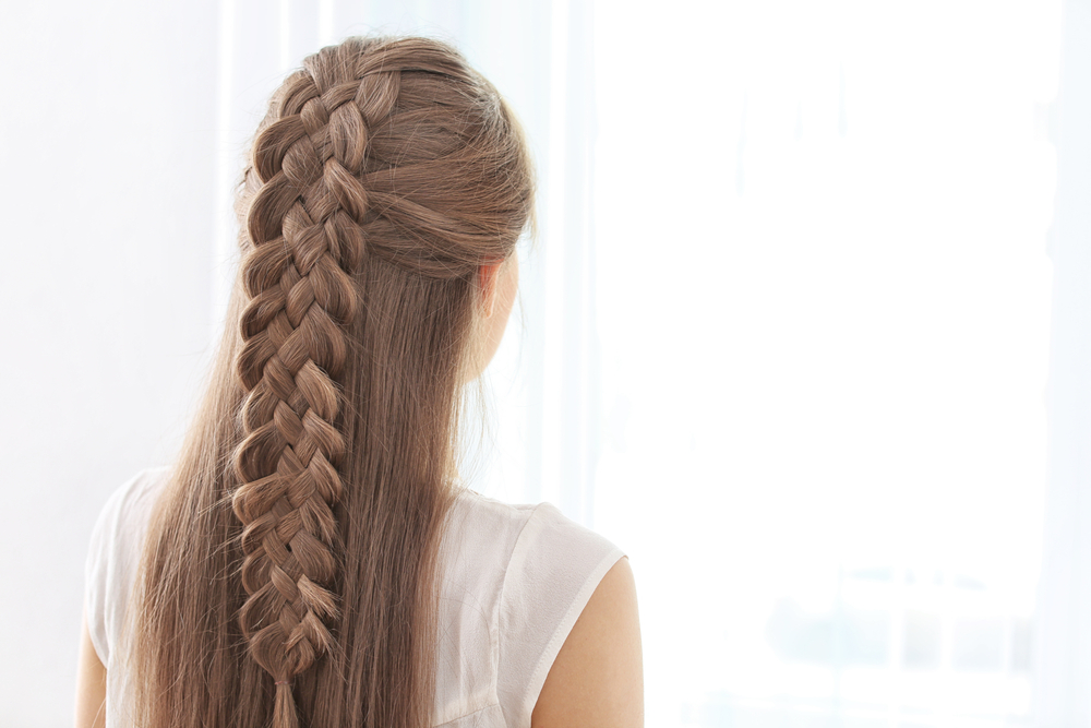 Achteraanzicht van brunette vrouw met ingewikkelde halve updo van 5 strengen vlecht staand voor raam