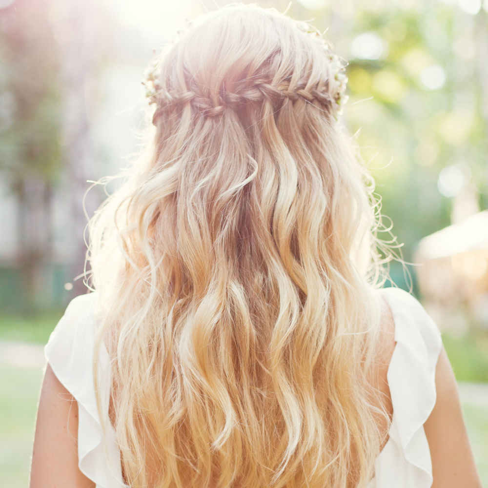 Blonde bruid in witte jurk draagt haar lange golvende haar in een half op half neer stijl met watervalvlecht