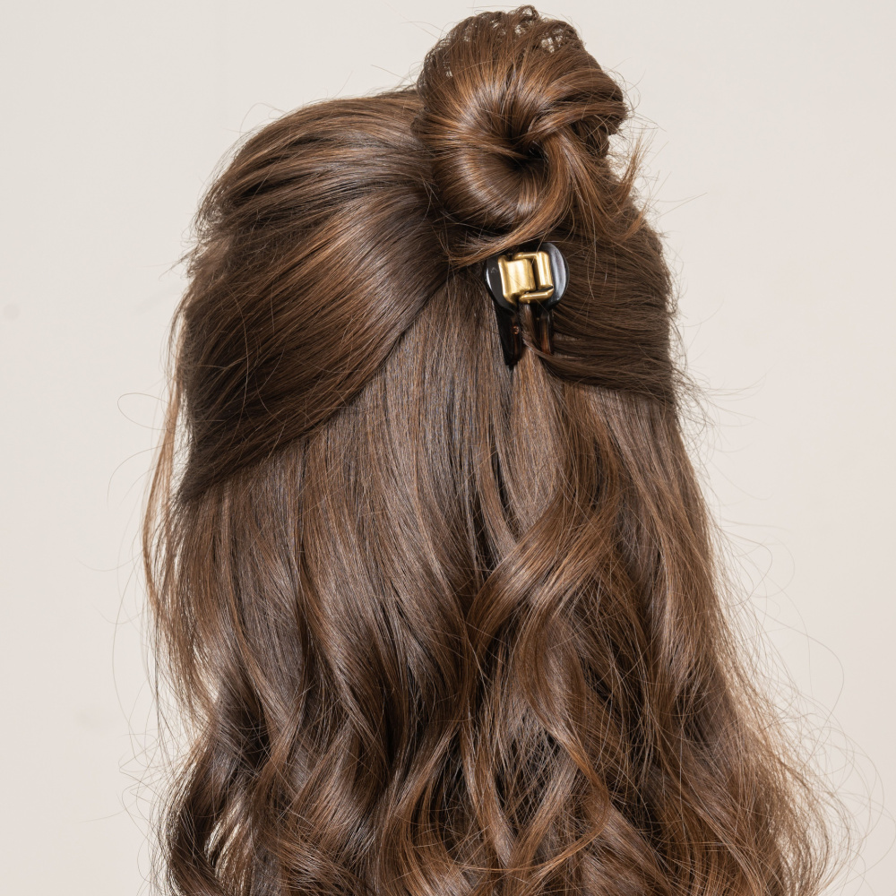 Achteraanzicht van vrouw met lang krullend brunette haar die een van de vele leuke half op half neer kapsels draagt met een haarklem en knotje