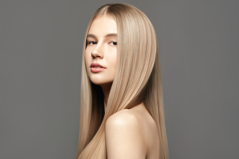 Vrouw met blote schouders voor grijze muur draagt haar haar steil in een van de beste tinten blond voor neutrale huidtinten, beige blond