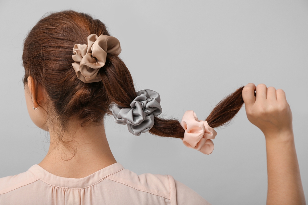 Achteraanzicht van vrouw met lang bruin haar gestyled in een scrunchy bubble braids kapsel dat de uiteinden van haar haar omhoog houdt voor een grijze muur.