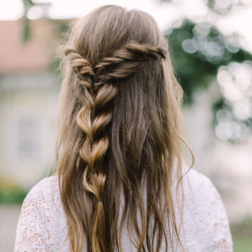 Achteraanzicht van vrouw in witte jurk die lang bruin haar draagt in half omhoog gedraaide bellenvlecht stijl