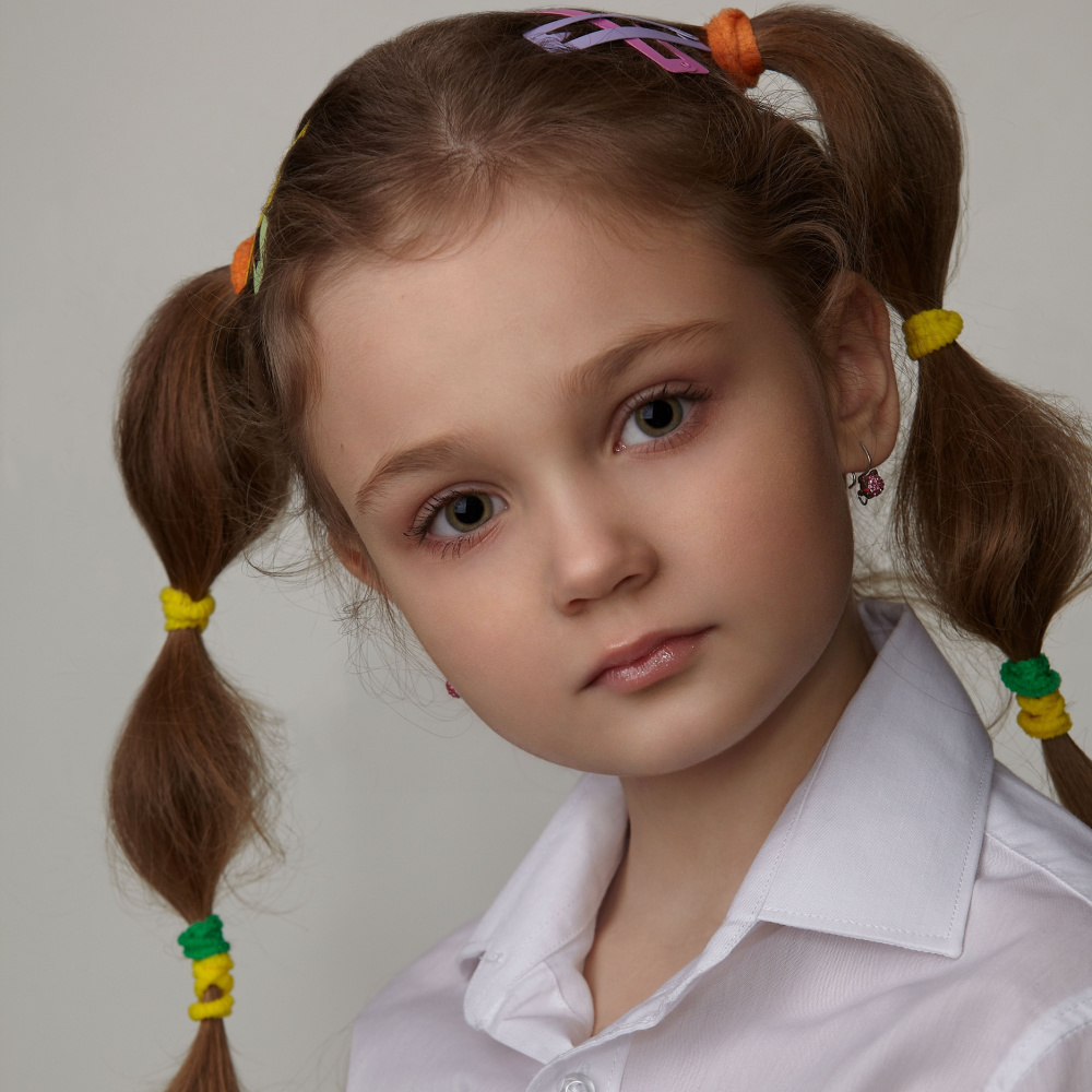 Klein meisje getoond van dichtbij met vlechtjes met kleurrijke elastieken en haarklemmen en een hemd met kraag.