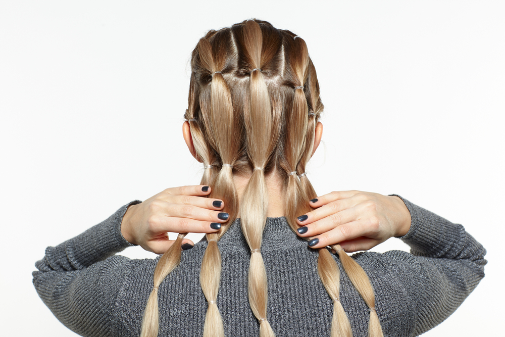 Blonde vrouw getoond van achteren met grijze lange mouwen en meerdere bubble braids gestyled over haar hele hoofd.