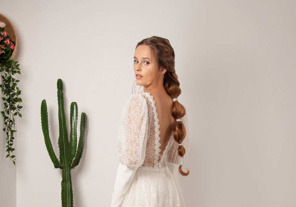 Vrouw in bruidsjurk kijkt over haar schouder terwijl ze een bubble braid kapsel op de rug draagt met cactus aan haar linkerzijde