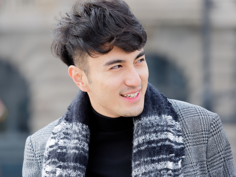 Glimlachende Koreaanse man draagt een jas en sjaal in de stad met een van de beste Koreaanse mannenkapsels, een volumineuze krullende look met burst fade