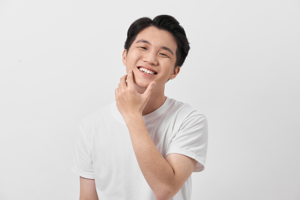 Koreaanse man legt zijn hand op zijn kin en draagt een wit t-shirt in een witte kamer met volumineus teruggeborsteld kapsel