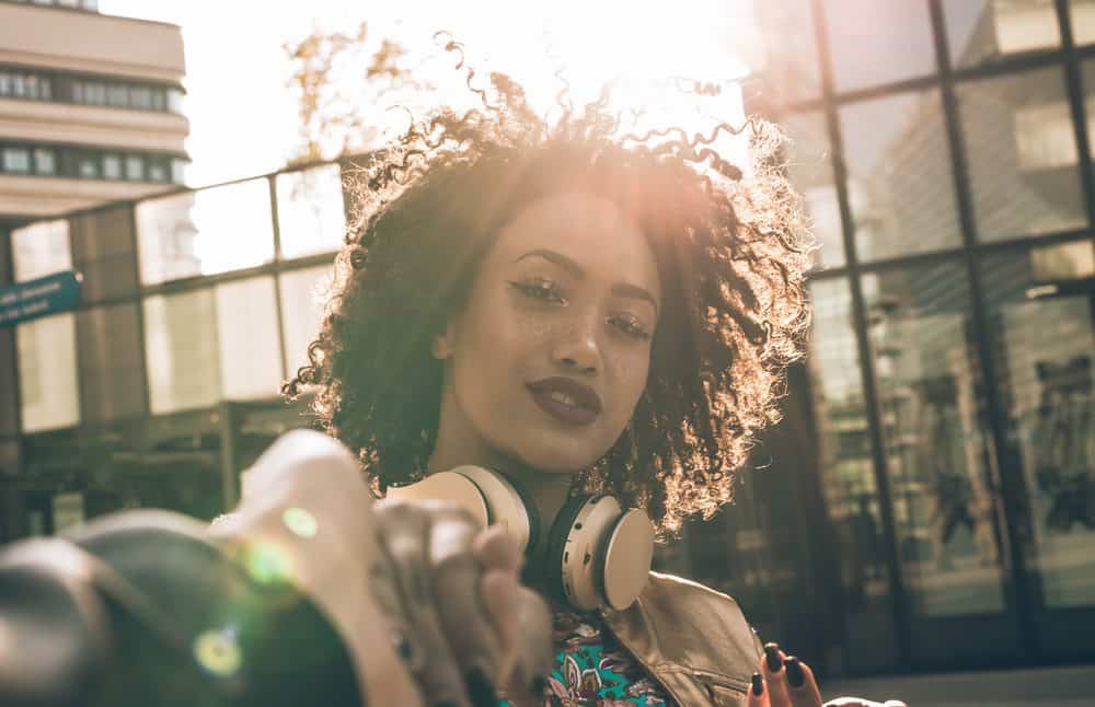 Latijnse vrouw met krullend haar dat geurde naar cederhoutolie en op een straathoek stond met een beats koptelefoon op.