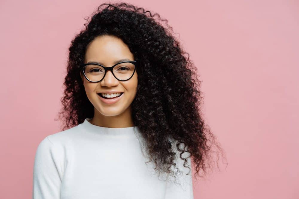 Jonge Afro-Amerikaanse vrouw die een witte trui draagt met type 3c krullende haarlokken. Haar haar is behandeld met bergamotolie.