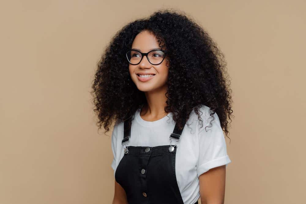 Leuke Amerikaanse vrouw die zwarte Tommy Hilfiger overalls draagt en een wit Hanes t-shirt met natuurlijk haar.