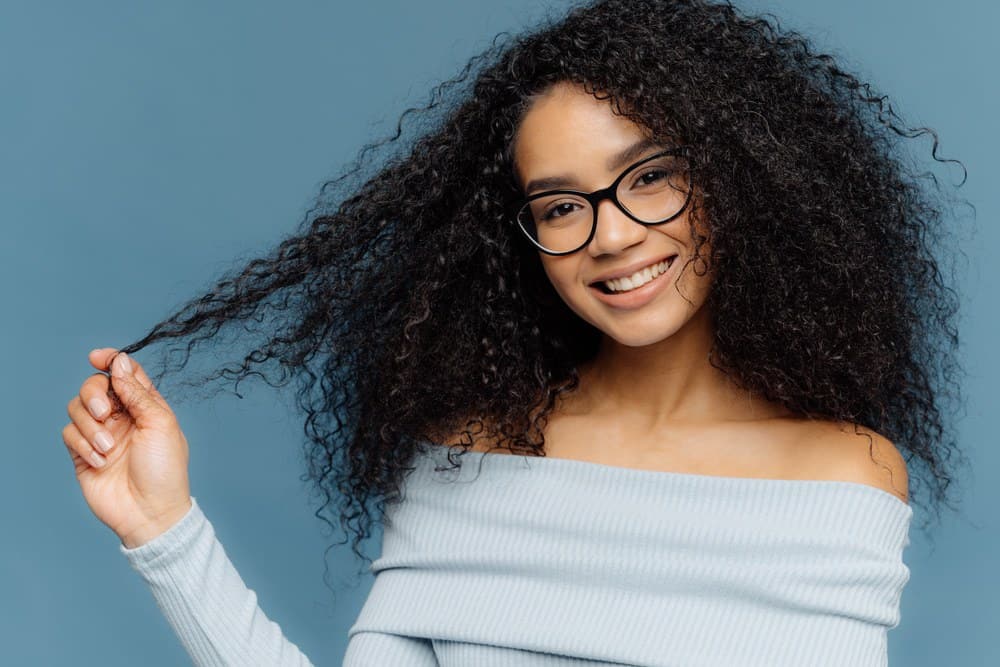 Afro-Amerikaanse vrouw van nature krullend type 3a haar dat is behandeld met bergamotolie voor haargroei met een blauwe trui en een leesbril.