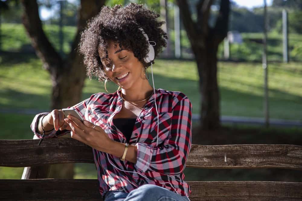 Jonge Afro-Amerikaanse vrouw die naar muziek luistert op mobiele telefoon.