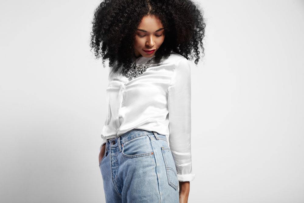 Amerikaanse vrouw met een wit zijden shirt, zilveren ketting, vervaagde blauwe jeans en rode lippenstift met golvend natuurlijk haar.