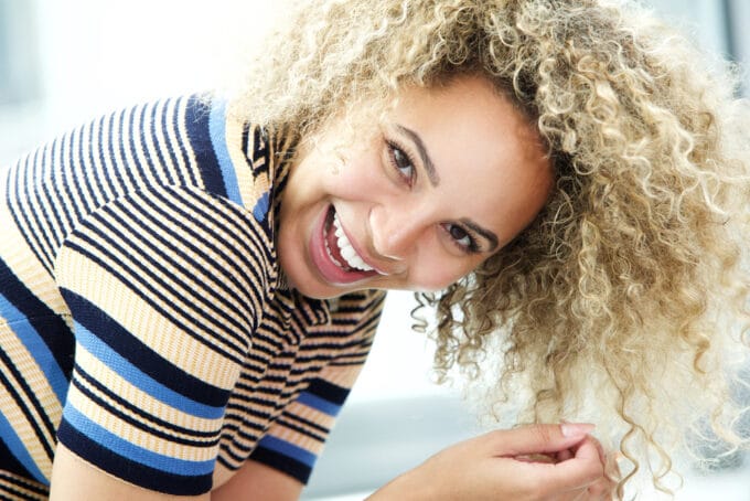 Amerikaanse vrouwen met ombre golven gestyled met permanente kleurstof dragen een zwart, geel en blauw getailleerde trui met korte mouwen met een enorme glimlach.