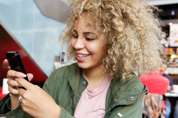 Vrouwen van gemengd ras die ombre krullend haar en een groen jasje dragen met een iPhone.