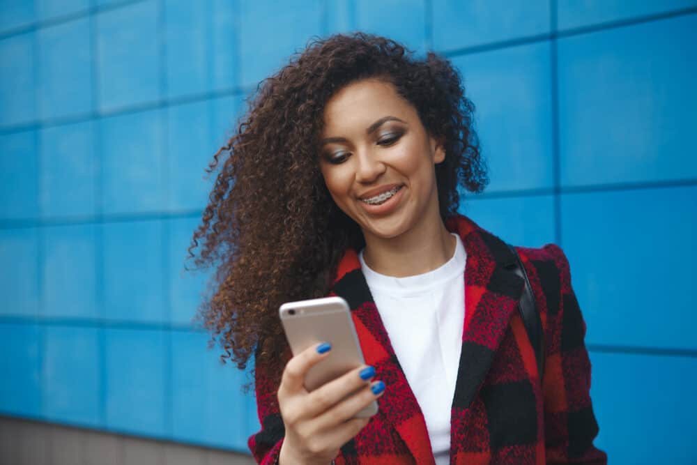 Afro-Amerikaanse vrouw die onderzoek doet naar dunner wordend haar en beschadigde haarporiën op haar iPhone