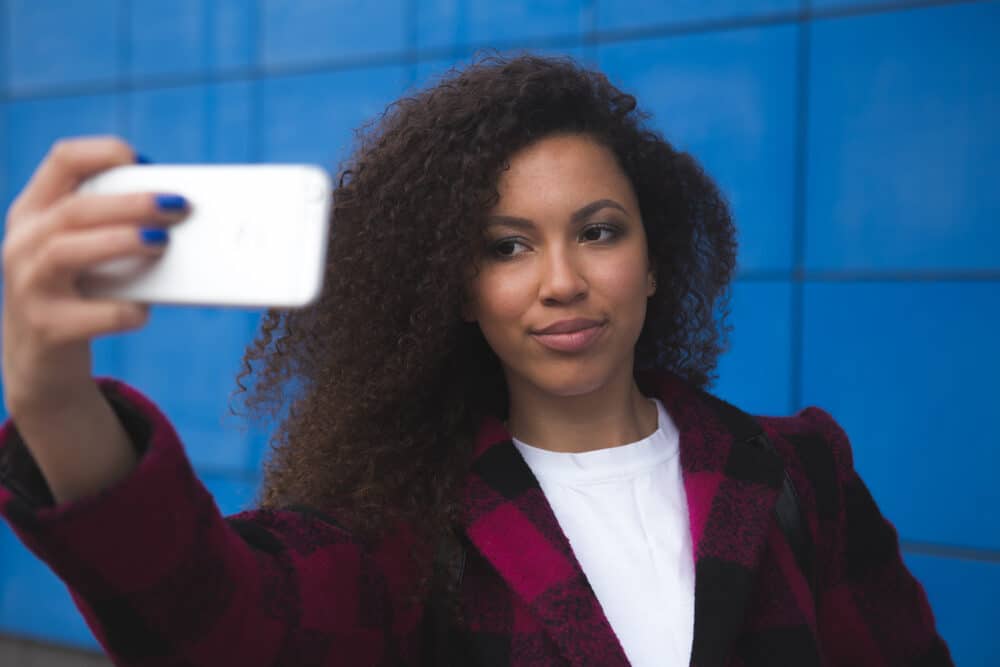 Gelukkige jonge vrouw die een iPhone 10s buiten gebruikt op een winderige lentedag.