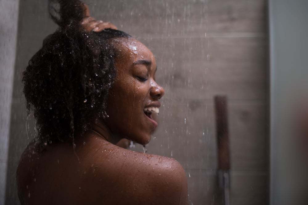 Vrouw die haar haar onder de douche wast met arganolie, kokosmelk en Curl Right Shampoo