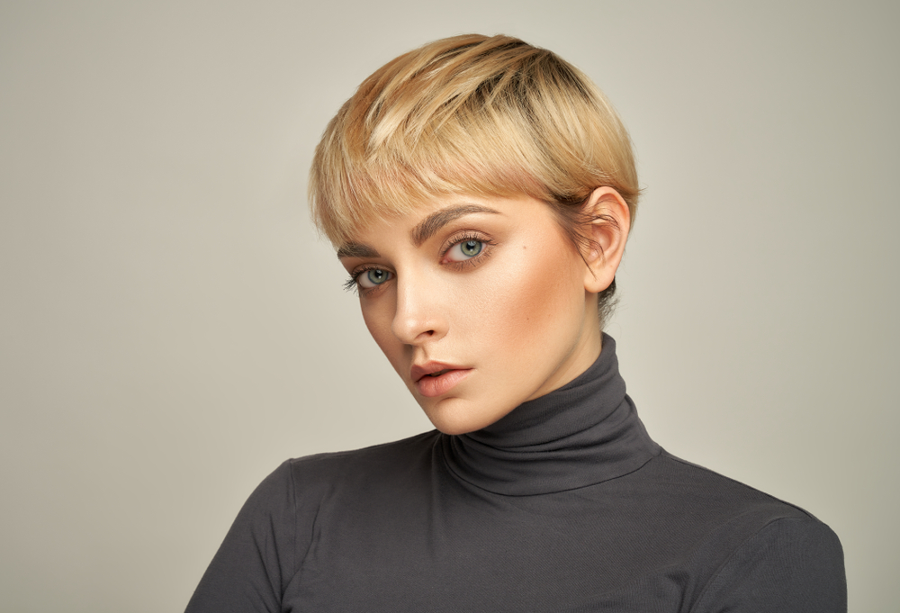 Vrouw met korte blonde pixie cut die een grijze coltrui draagt is een voorbeeld van grote hartvormige gezichtskapsels 