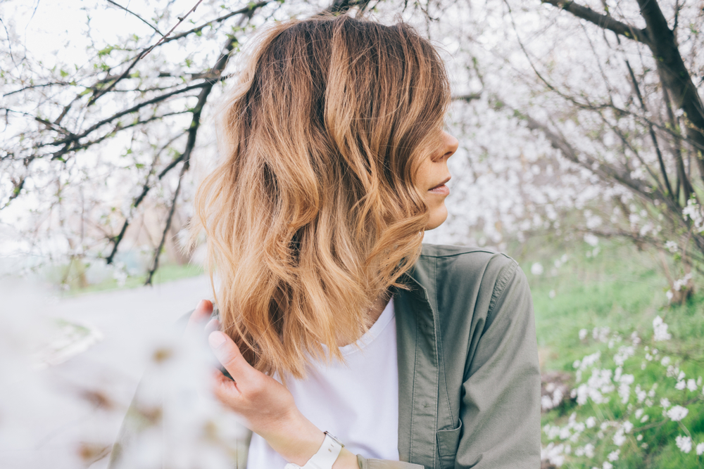 Zijaanzicht van blonde vrouw met halflang gelaagd haar gestyled met golven terwijl ze buiten zit 