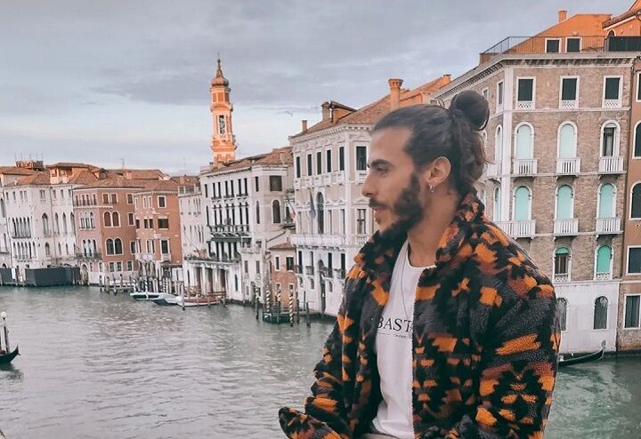 Man met een Man Bun kapsel zittend op een brug in Venetië