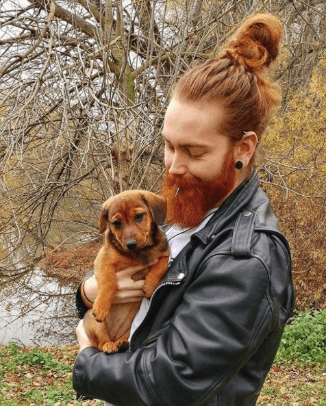 vooraanzicht van een man met rood haar in een bovenste knoop met een volle baard die een puppy vasthoudt