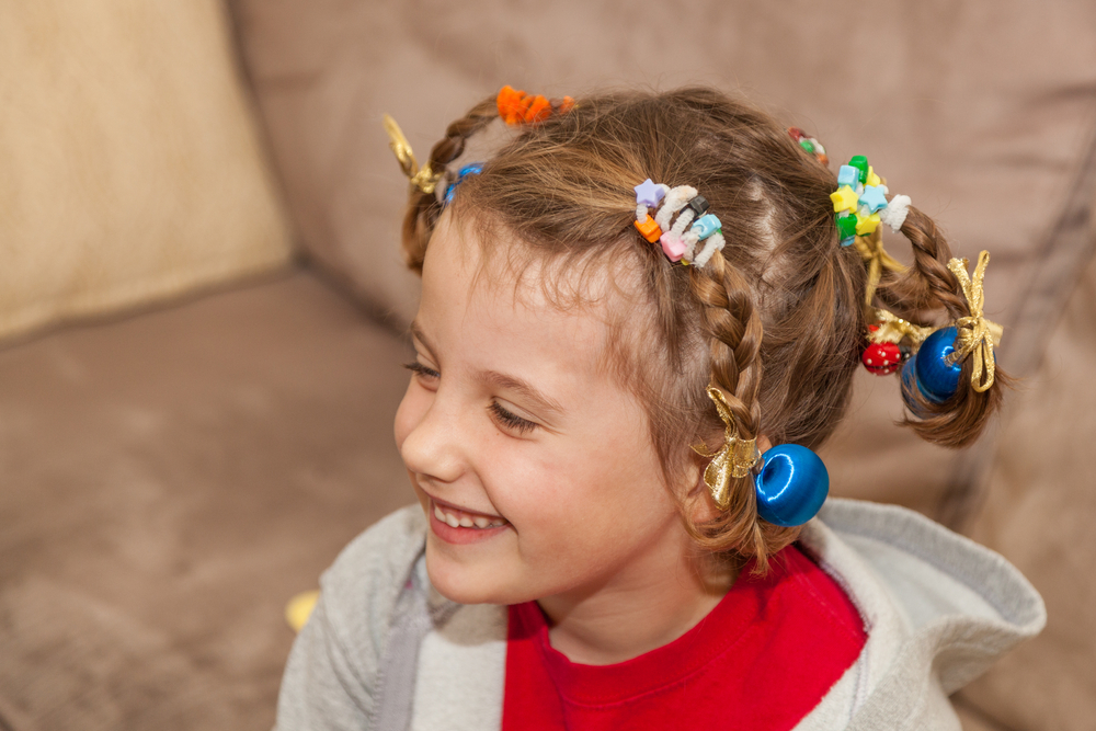 Klein meisje glimlacht met gesloten ogen en draagt meerdere vlechten beveiligd met kleurrijke haaraccessoires voor een stuk op gekke haardag ideeën