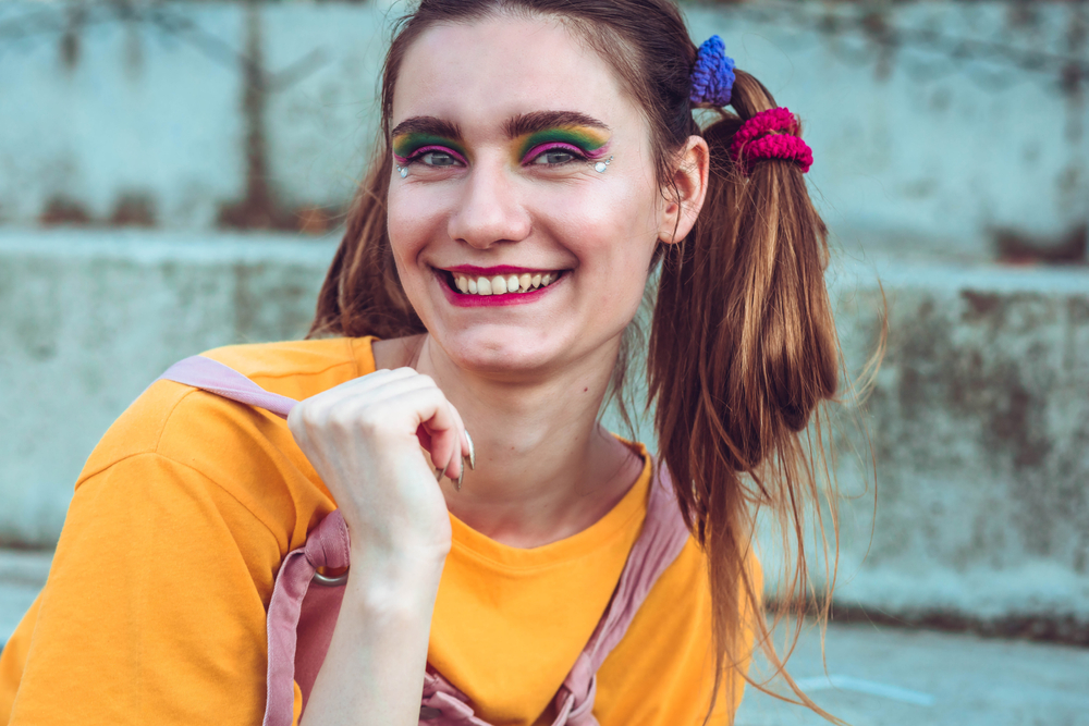 Jonge vrouw met haar gestyled in gekke varkensstaart knotten draagt heldere oog make-up buiten met oranje shirt aan