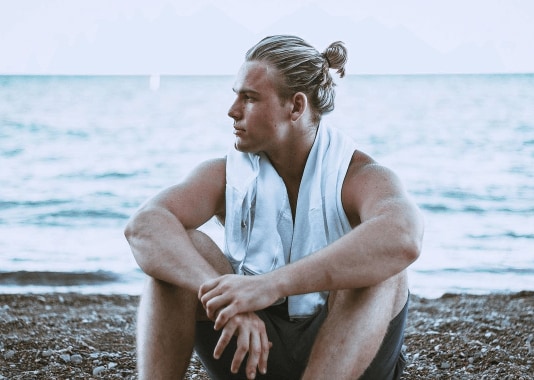 Viking Hairstyles: Man die op het strand zit met blond haar in een mannen knot