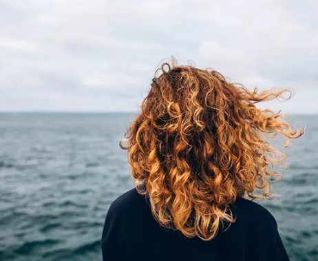 Vrouw op het strand met krullen verkregen door zeezout op het haar te spuiten