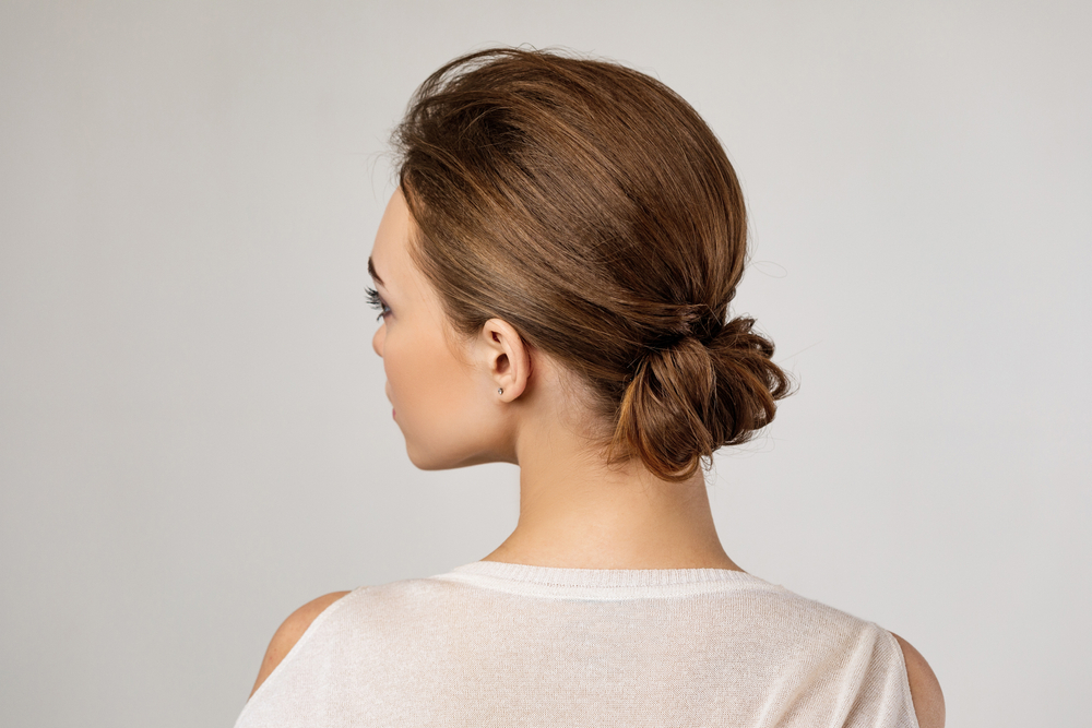 Voor een stuk over halflange gelaagde kapsels voor vrouwen boven de 50, draagt een vrouw een chignon knot en kijkt naar links, gezien van achteren.