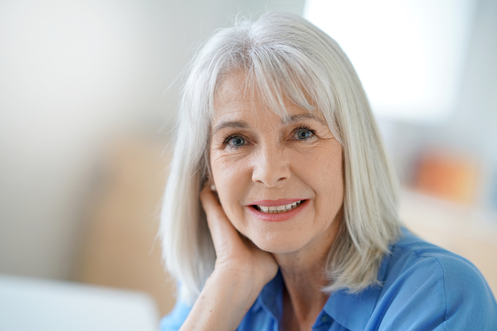 Off-Center Part With Bangs and Short Layers, een geweldig halflang kapsel voor vrouwen boven de 50, afgebeeld op een vrouw in een blauw spijkerblouse.