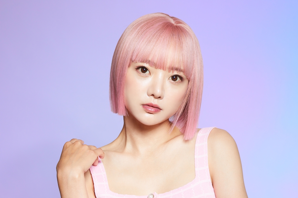 Licht Bubblegum Roze haar op een Koreaanse vrouw met grote bruine ogen in een pastel paarse kamer.