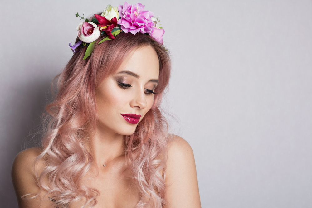 Vrouw met ombre lichtroze haar die een gebloemde hoofdband draagt, een diamanten halsketting en rode lippenstift in een zilveren kamer