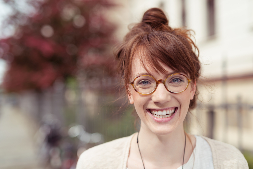 Messy Top Knot With Layered Side-Swept Bangs op een vrouw die groot glimlacht met een wazige achtergrond