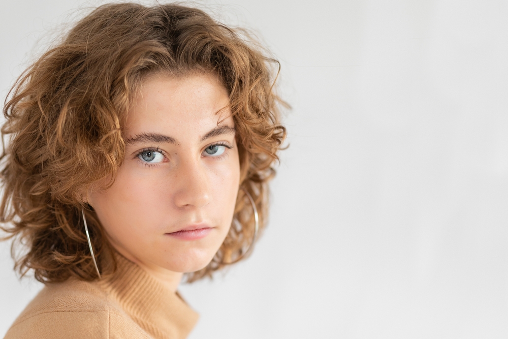 Tomboy met een pluizig en krullend pageboy kapsel die hoepel oorbellen draagt en naar de camera kijkt in een studio