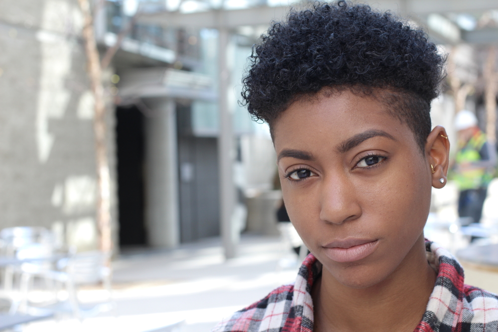 Serieuze Afro-Amerikaanse vrouw kijkt naar de camera met een kort midden kapsel en geruit shirt op een stadsstraat voor een stuk over de nieuwe Brittney Griner kapselstijl