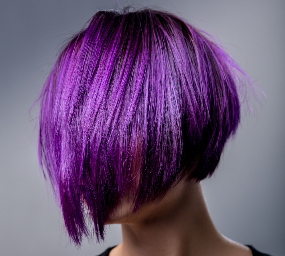 Vrouw met violet haar geborsteld over haar gezicht pronkt met een korte pixie bob kapsel met levendige kleur voor grijze achtergrond