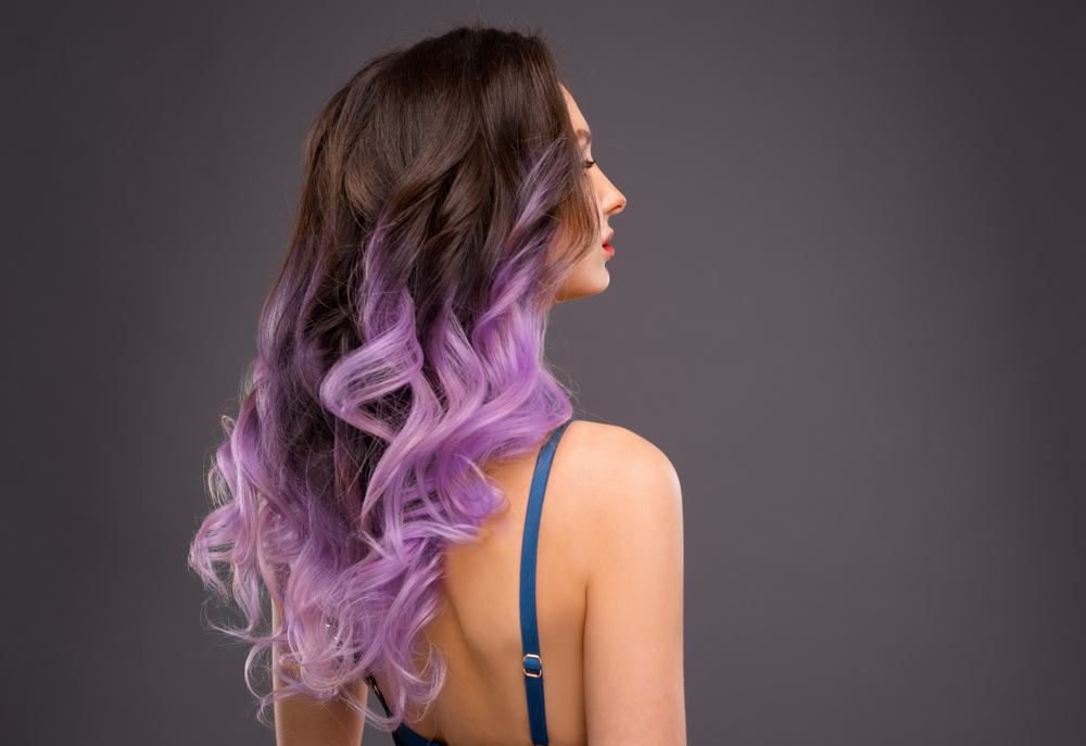 Achteraanzicht van vrouw met lang brunette haar en lavendel balayage kleur in een spaghetti band topje voor houtskool wand