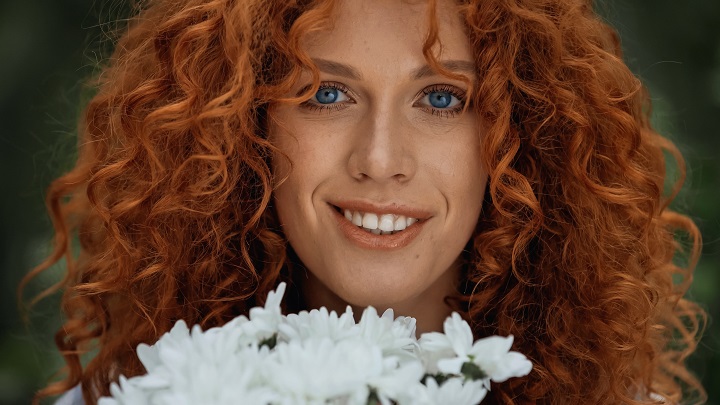 Glimlachende vrouw met blauwe ogen en golvend oranje haar