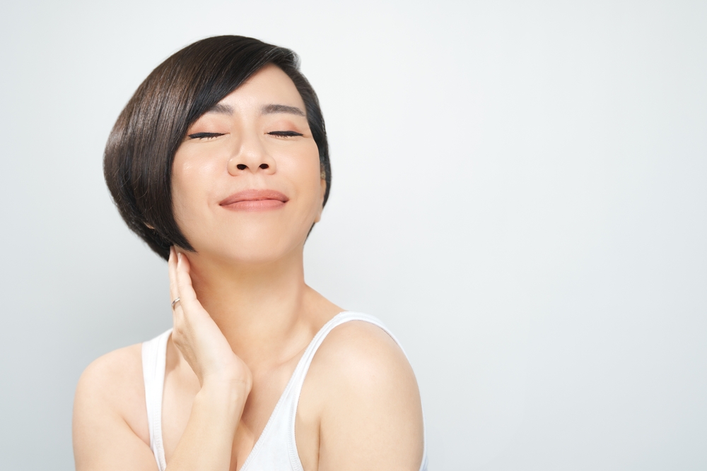 Aziatische vrouw in een witte tanktop glimlacht met gesloten ogen en pronkt met een van de verschillende kapsels voor vrouwen boven de 40 met een volumineuze bixie-snit