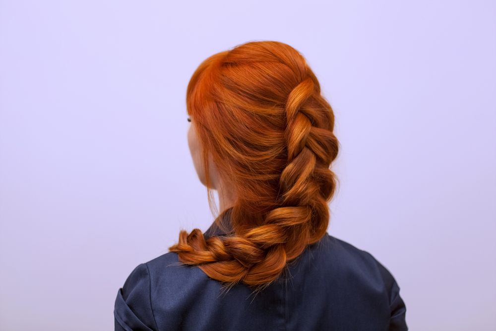 Achteraanzicht van een vrouw met rood haar die een van onze favoriete kapsels voor vrouwen boven de 40 draagt met een enkele Nederlandse vlecht over haar schouder gedrapeerd