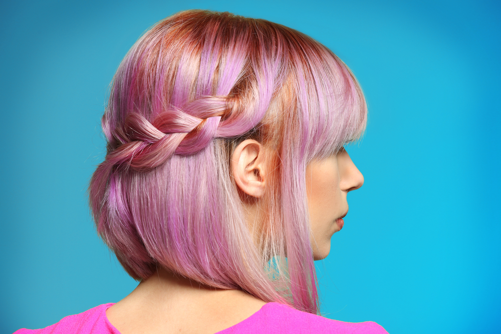 Jonge vrouw met paarse haarkleur draagt een half opgetrokken vlechtkapsel perfect voor prom voor blauwe muur