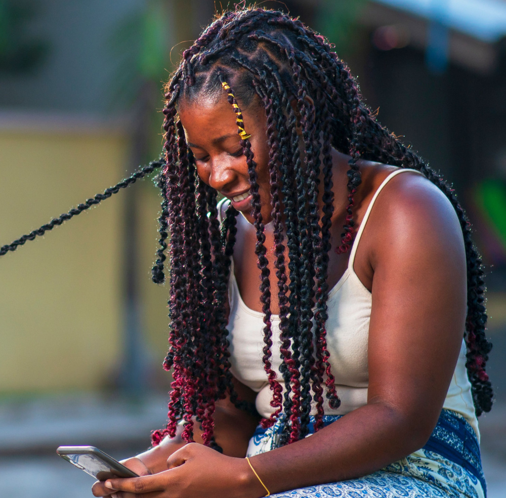 Afro-Amerikaanse vrouw glimlacht naar haar telefoon terwijl ze lentewendingen probeert, een van de beste schattige zwarte kapsels