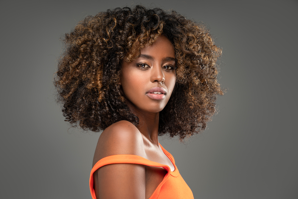 Afro-Amerikaanse vrouw met oranje tanktop draagt een voorbeeld van schattige zwarte kapsels met losse spoelen en balayagekleur