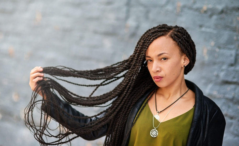 Vrouw in groen overhemd en zwart vest houdt haar lange haar uit om te pronken met de Senegalese twists kapsel